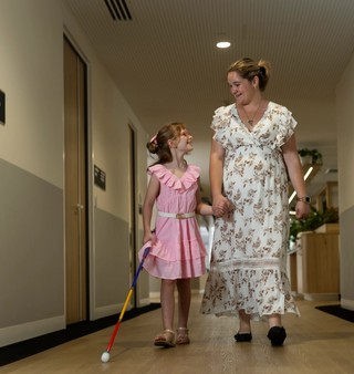 A mother walking with her daughter who is using a white cane.