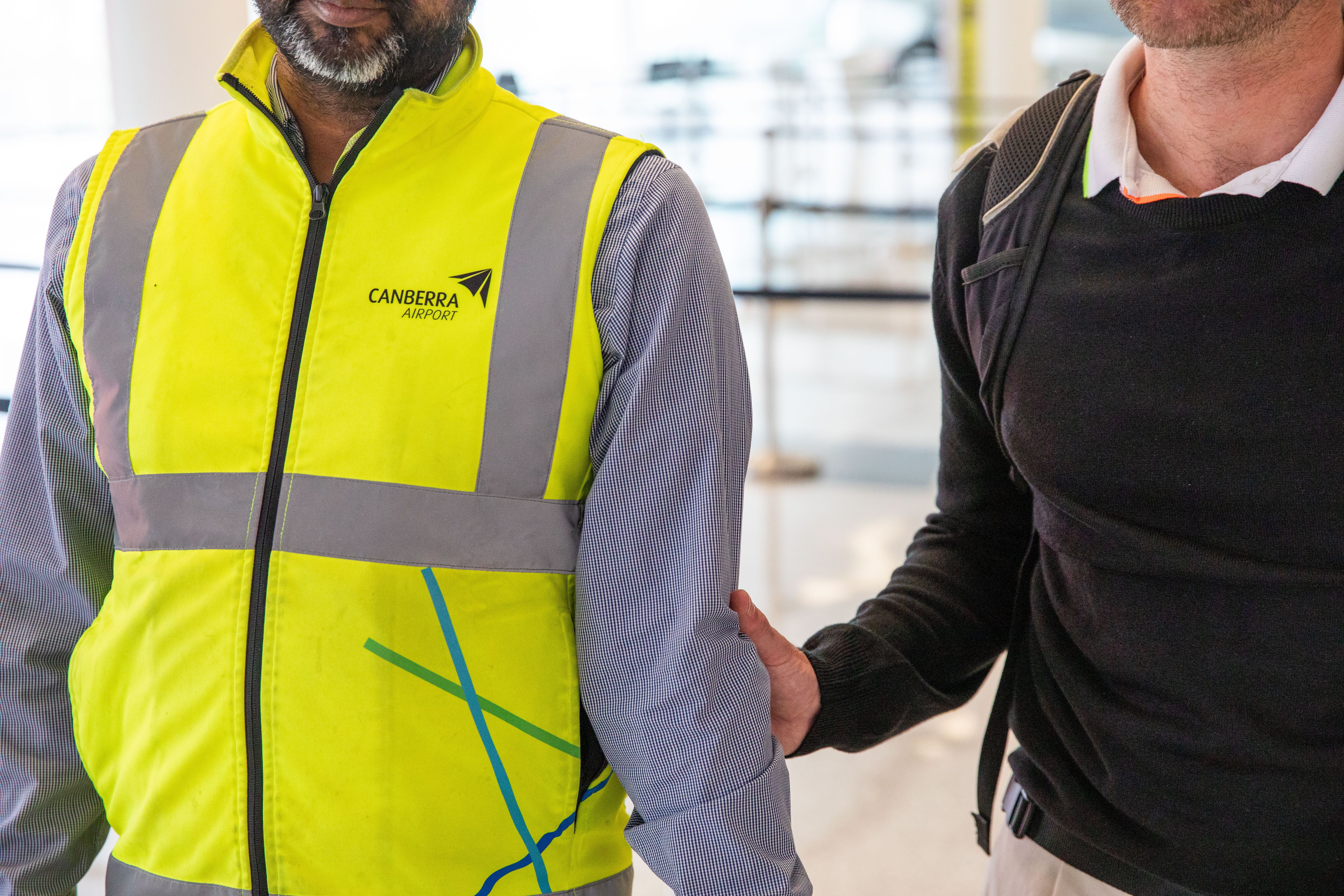 A close up of an airport staff member guiding a Handler and his Guide Dog.