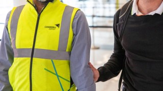 A close up of an airport staff member guiding a Handler and his Guide Dog.