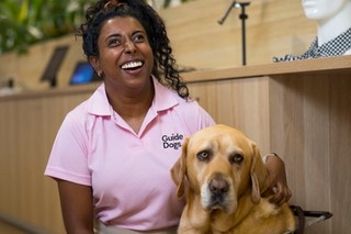 Abby sitting with her Guide Dog Duke and smiling.