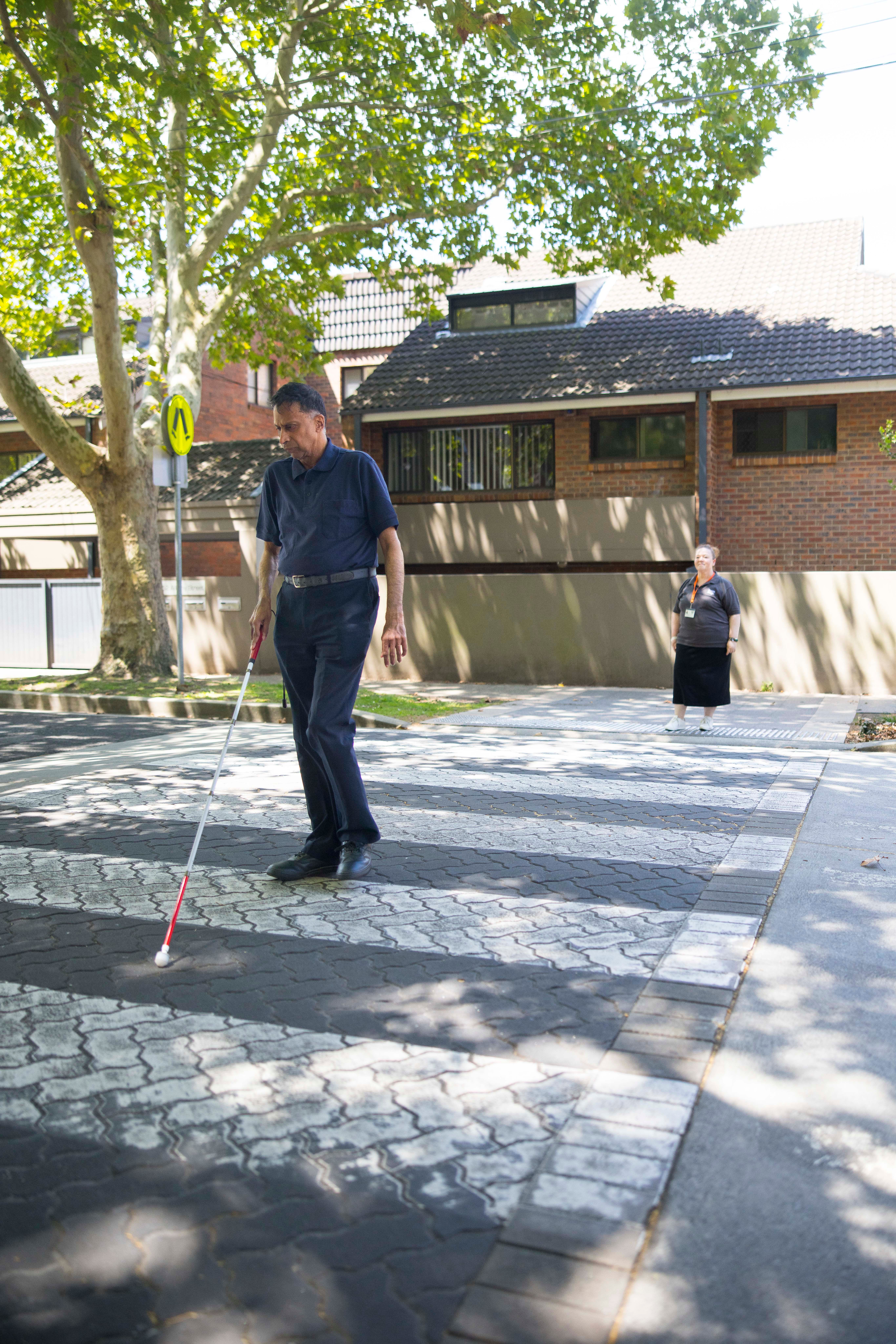 A Client crossing a pedestrian crossing with a cane.