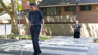 A Client crossing a pedestrian crossing with a cane.