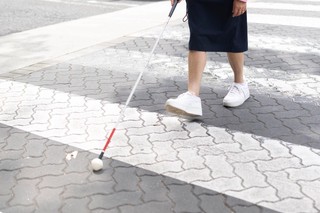 A Person walking with their cane across the pedestrian crossing.
