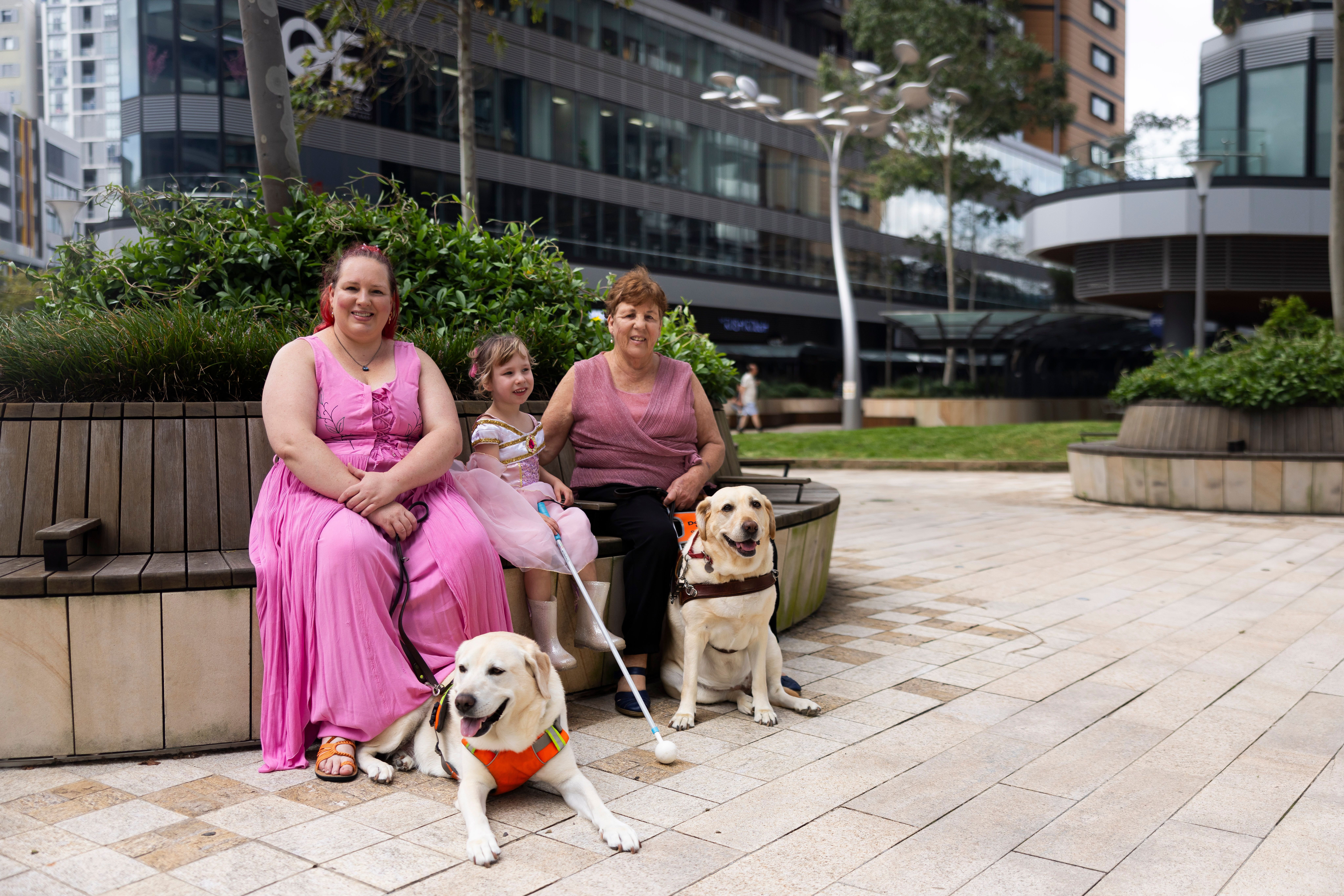 Three people sitting with their Guide Dogs and their canes.