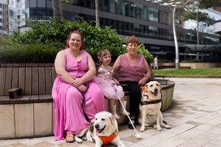 Three people sitting with their Guide Dogs and their canes.