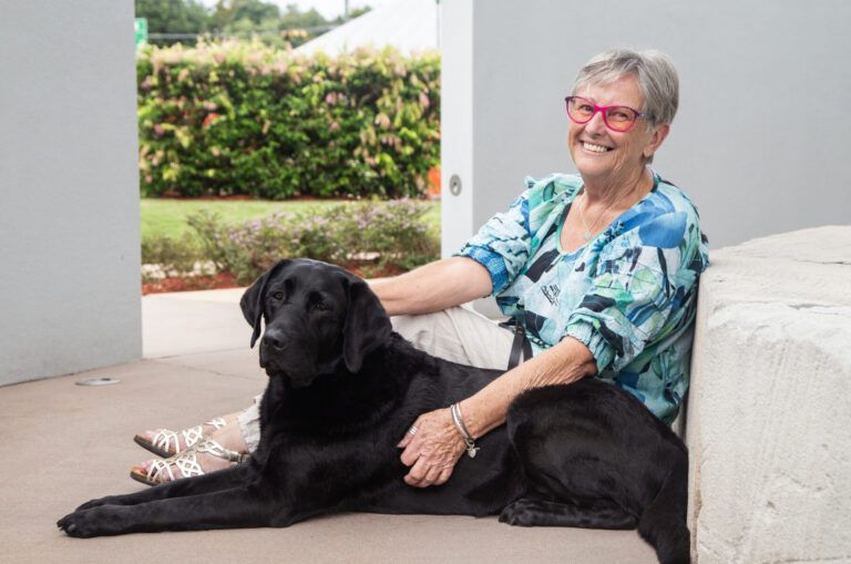 A person sitting with a black Labrador.
