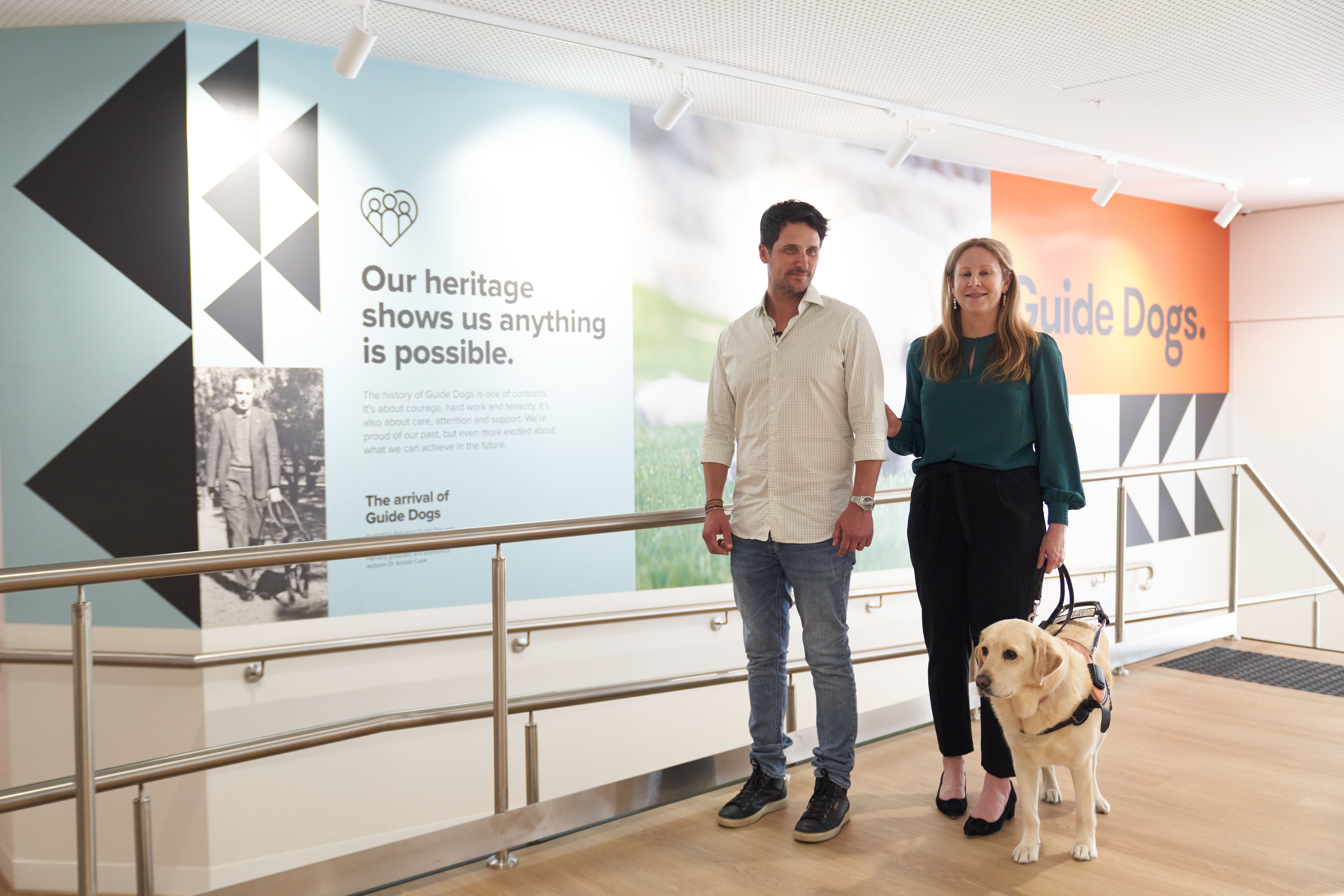 A person guiding a Guide Dog Handler and their Guide Dog.