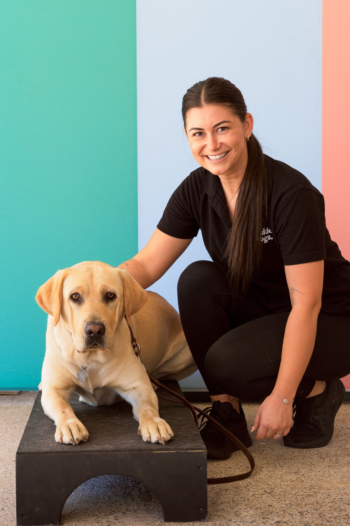 A person kneeling next to Clifford a yellow Labrador.