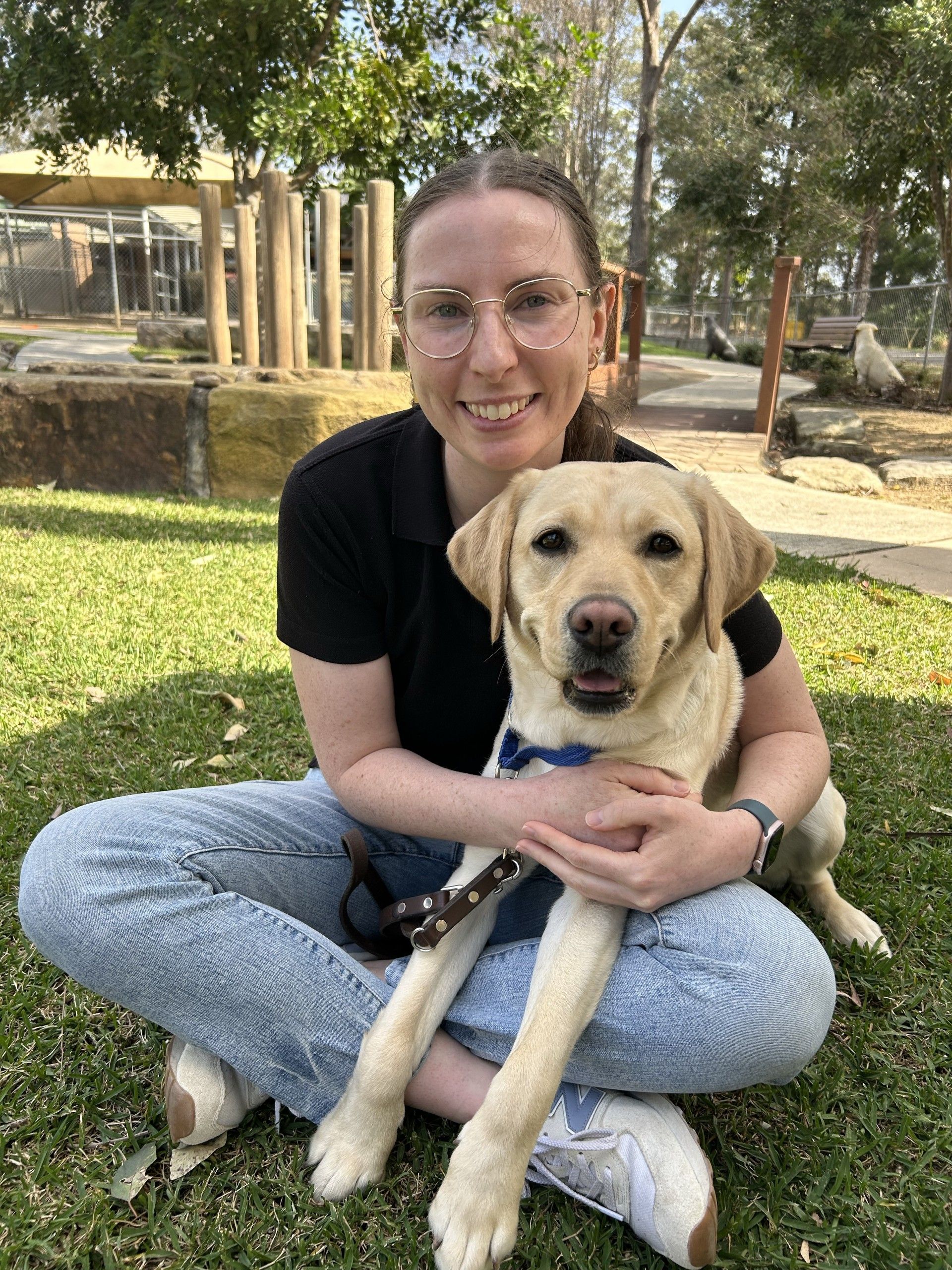Liz sits outside and smiles with a yellow Labrador on her lap. 