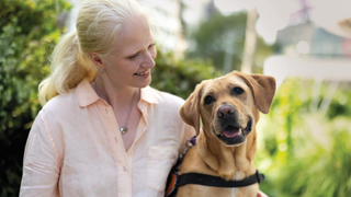 A woman sits outside with her yellow Labrador Guide Dog