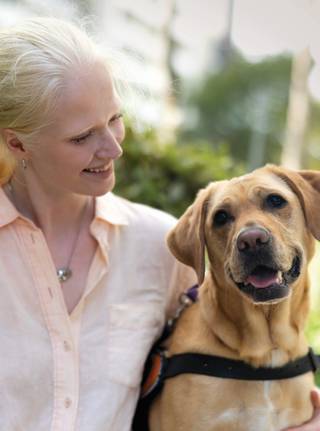 A woman sits outside with her yellow Labrador Guide Dog