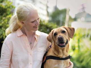 A woman sits outside with her yellow Labrador Guide Dog