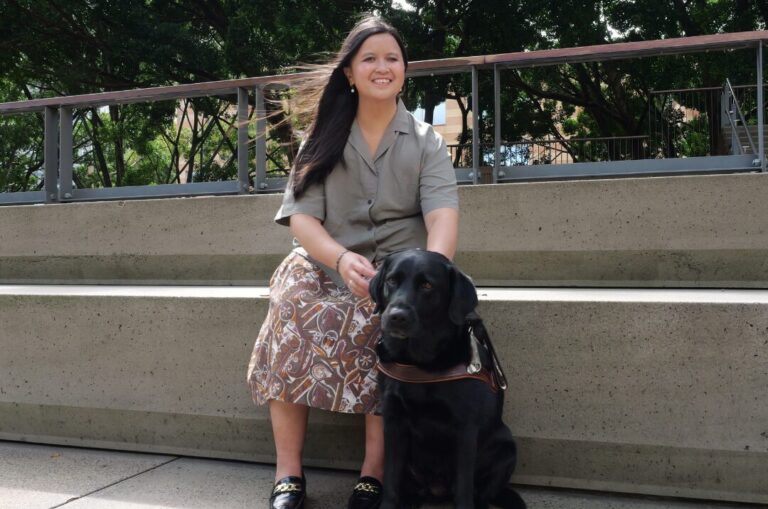 Rita sitting next to her black Labrador Guide Dog Triniti. 
