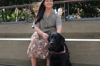 Rita sitting next to her black Labrador Guide Dog Triniti.