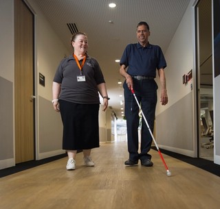 A staff member walking with a Client who is using a white cane.