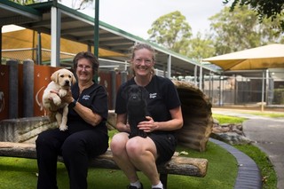 Two volunteers sitting with puppies smiling at the camera.