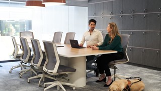 Two people sitting at a desk with a Guide Dog.