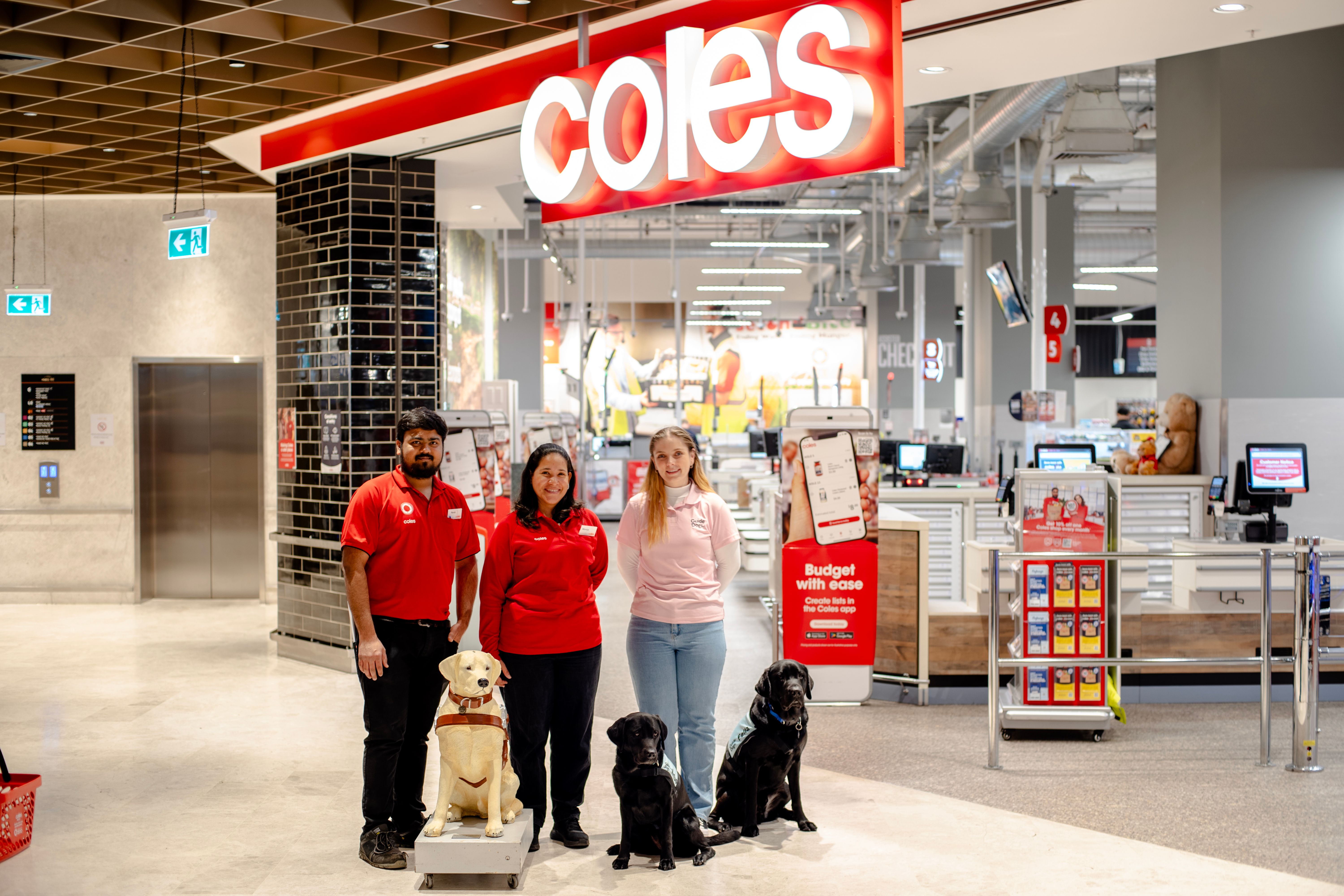 Coles and Guide Dogs Staff standing next to a Donation Dog statues with two black Labradors.