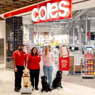Coles and Guide Dogs Staff standing next to a Donation Dog statues with two black Labradors.