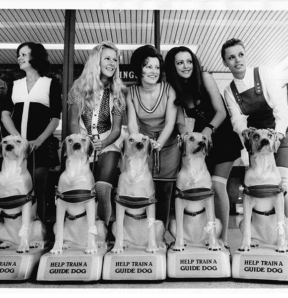 Black and white image of five women standing behind donation dogs.