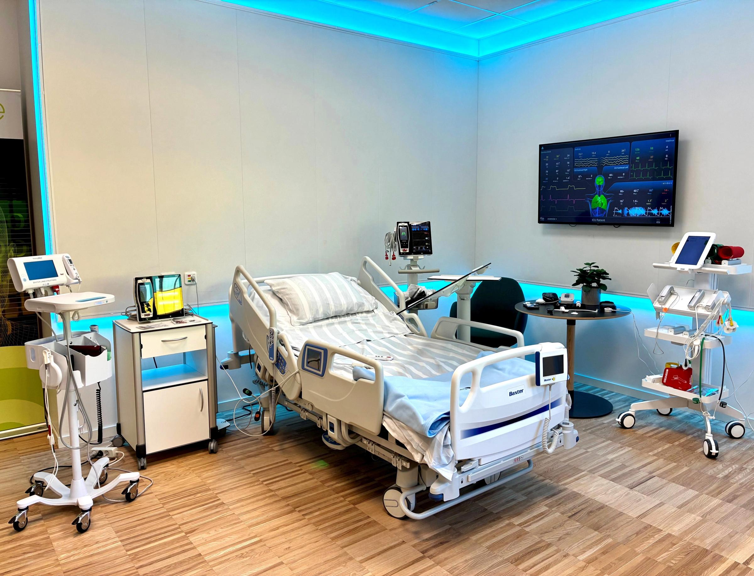 Sjukhusrum med en sjukhussäng i mitten. På båda sidor om sängen visas medicinsk utrustning. På ena väggen sitter en skärm som visar vitala parametrar.
