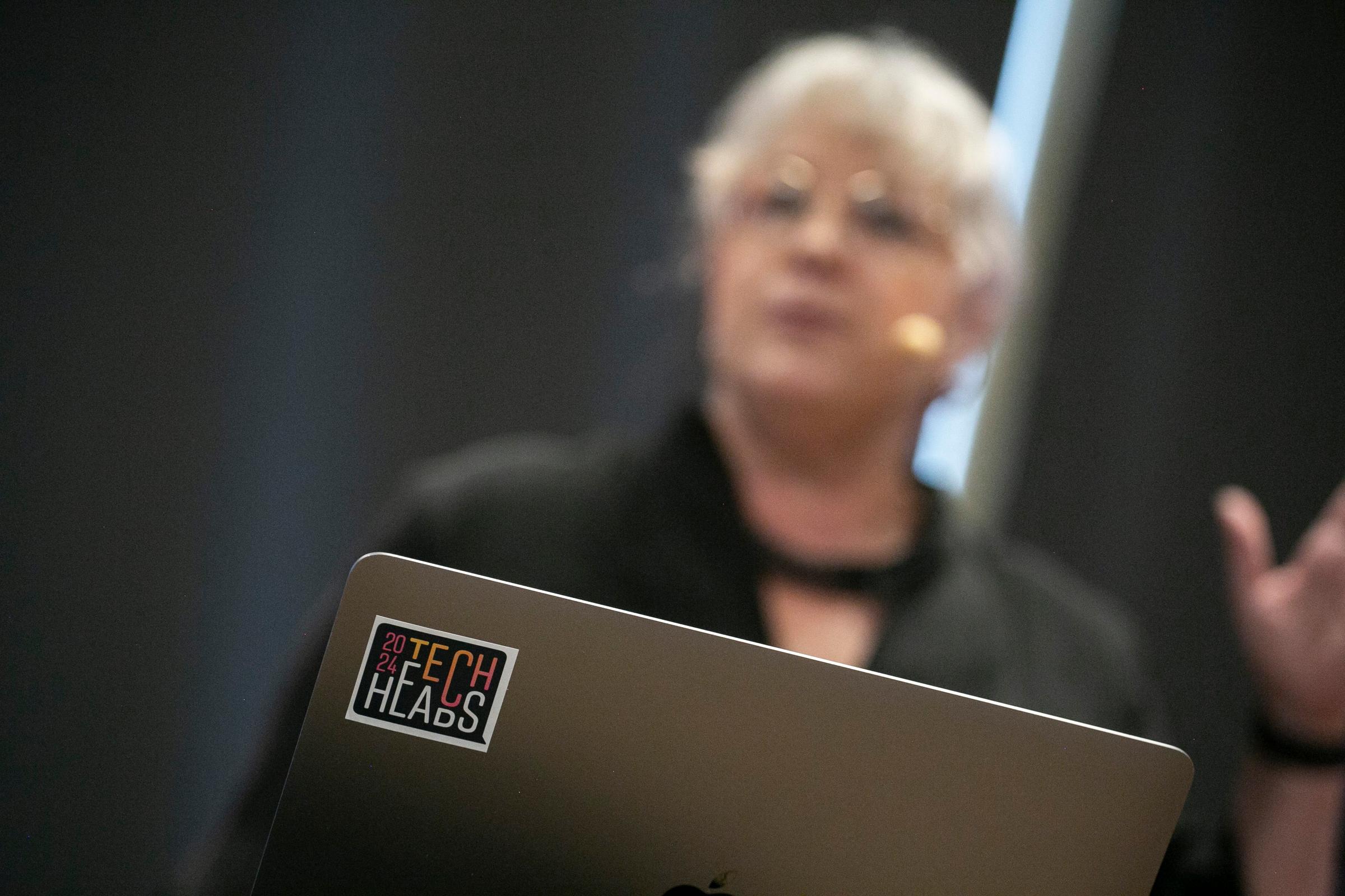 Dator med klistermärke "Tech Heads" i förgrund och talare Anna Olsson i bakgrund