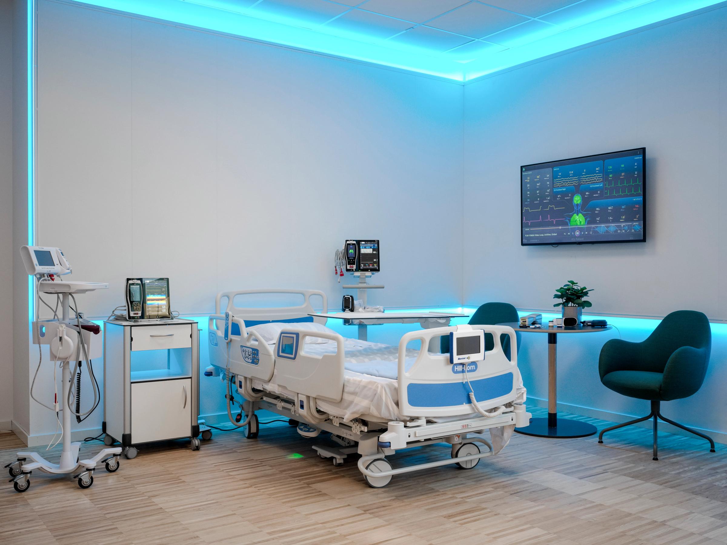 Sjukhusrum med en sjukhussäng i mitten. På båda sidor om sängen visas medicinsk utrustning. På ena väggen sitter en skärm som visar vitala parametrar.