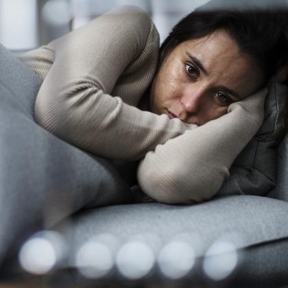 Woman resting her head on her arms on a couch, looking sad or thoughtful.