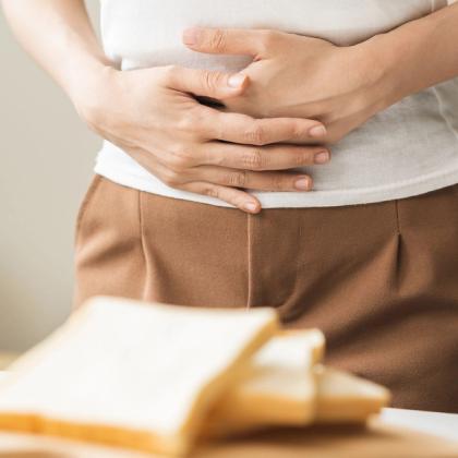 Woman holding her stomach in discomfort with sliced bread on a plate in the foreground, suggesting food intolerance or digestive issues.