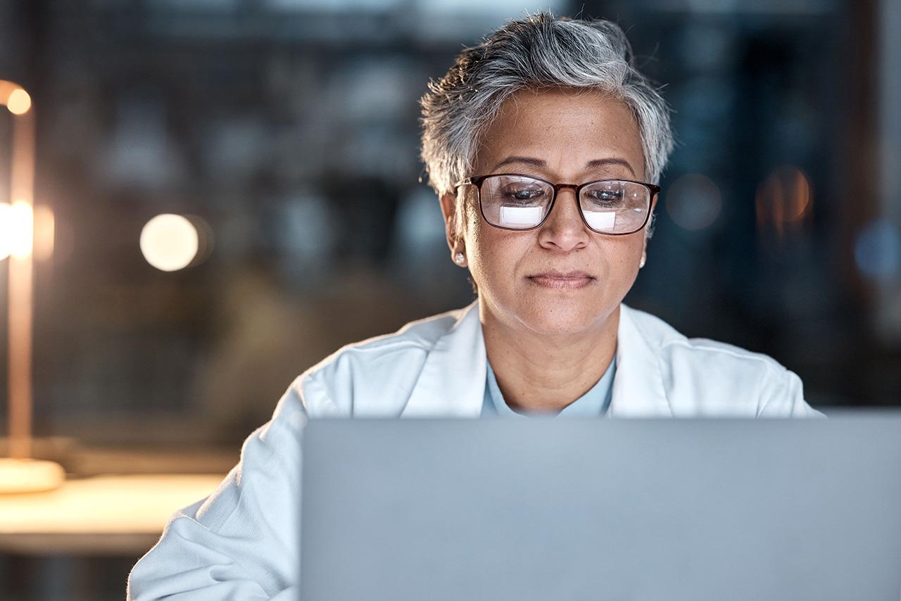 Mature woman with glasses using laptop in a dimly lit office setting