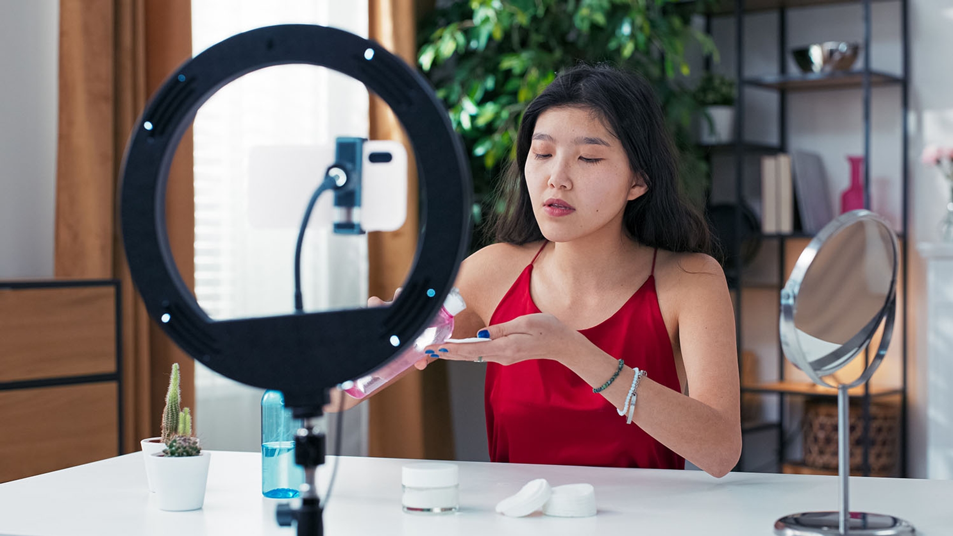 Young woman demonstrating a skincare routine while recording a video with a ring light and smartphone.