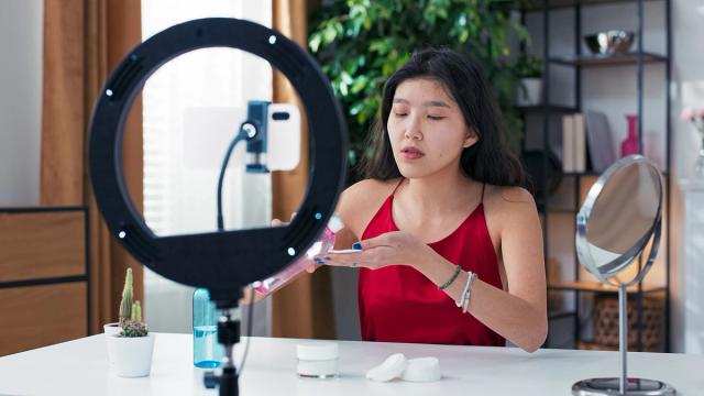 Young woman demonstrating a skincare routine while recording a video with a ring light and smartphone.