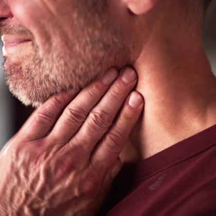 A man with stubble feels his neck.