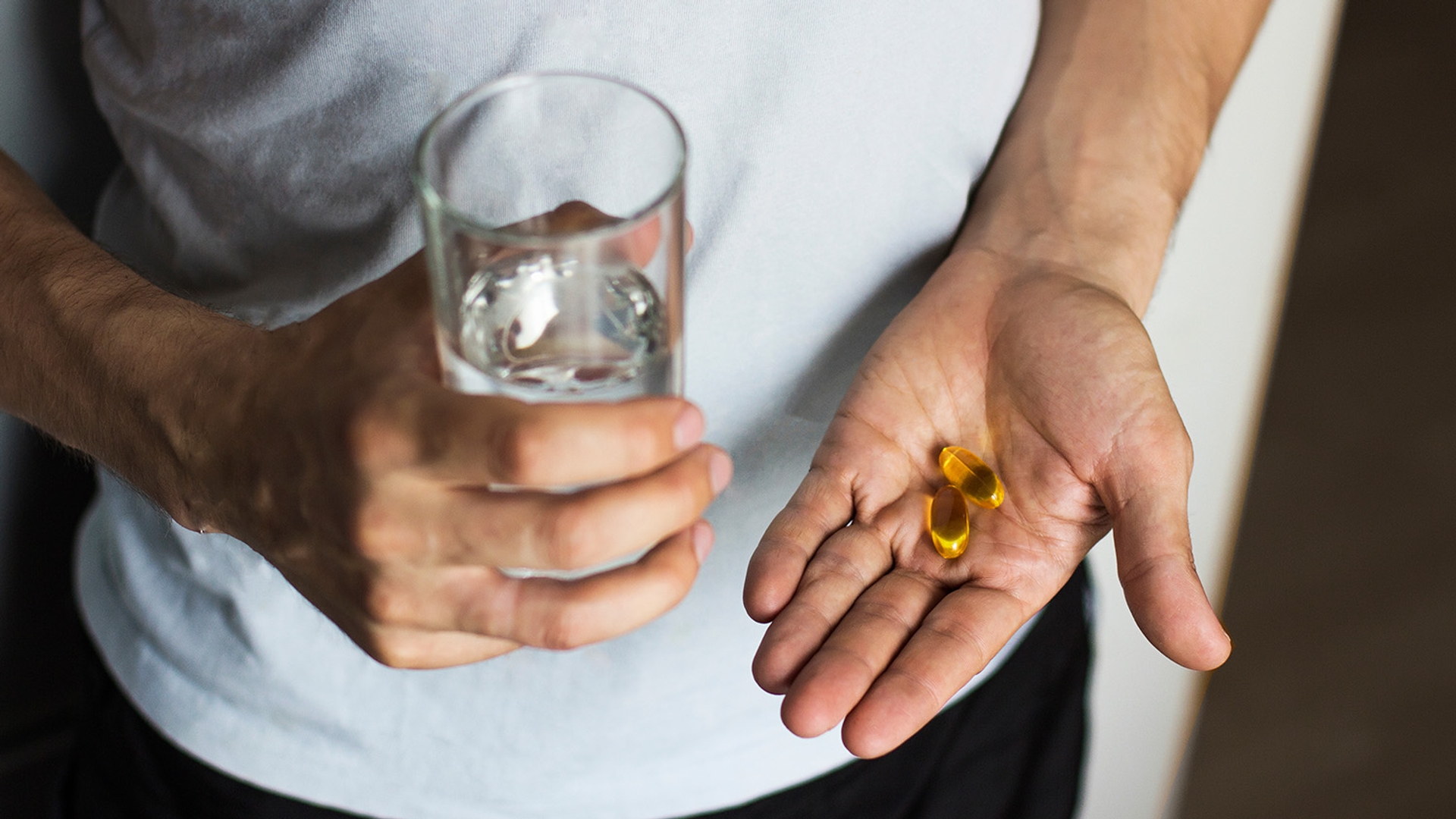 Close-up of a man's hands holding a glass of water and fish oil capsules