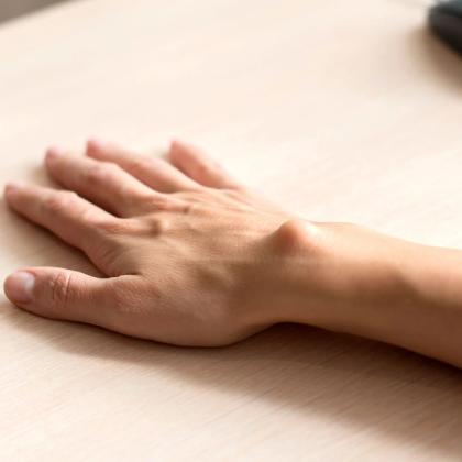 Close-up of a human hand resting on a wooden desk near a computer mouse
