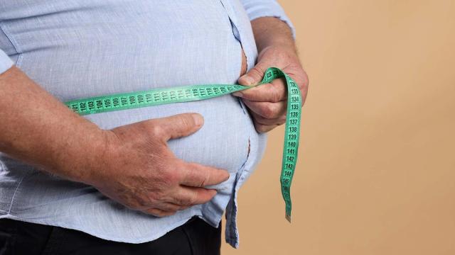Overweight person measuring their waist with a green tape measure.