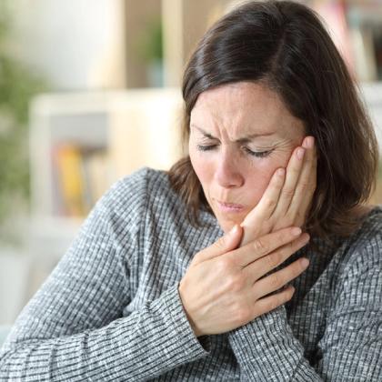Adult woman experiencing severe toothache or jaw pain, holding her cheek, feeling distressed