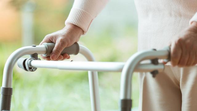 Close-up of an elderly person's hands holding a walker.