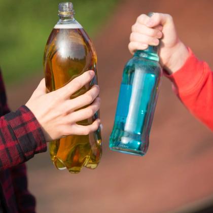 Two people clinking large bottles of amber and blue liquid outdoors.