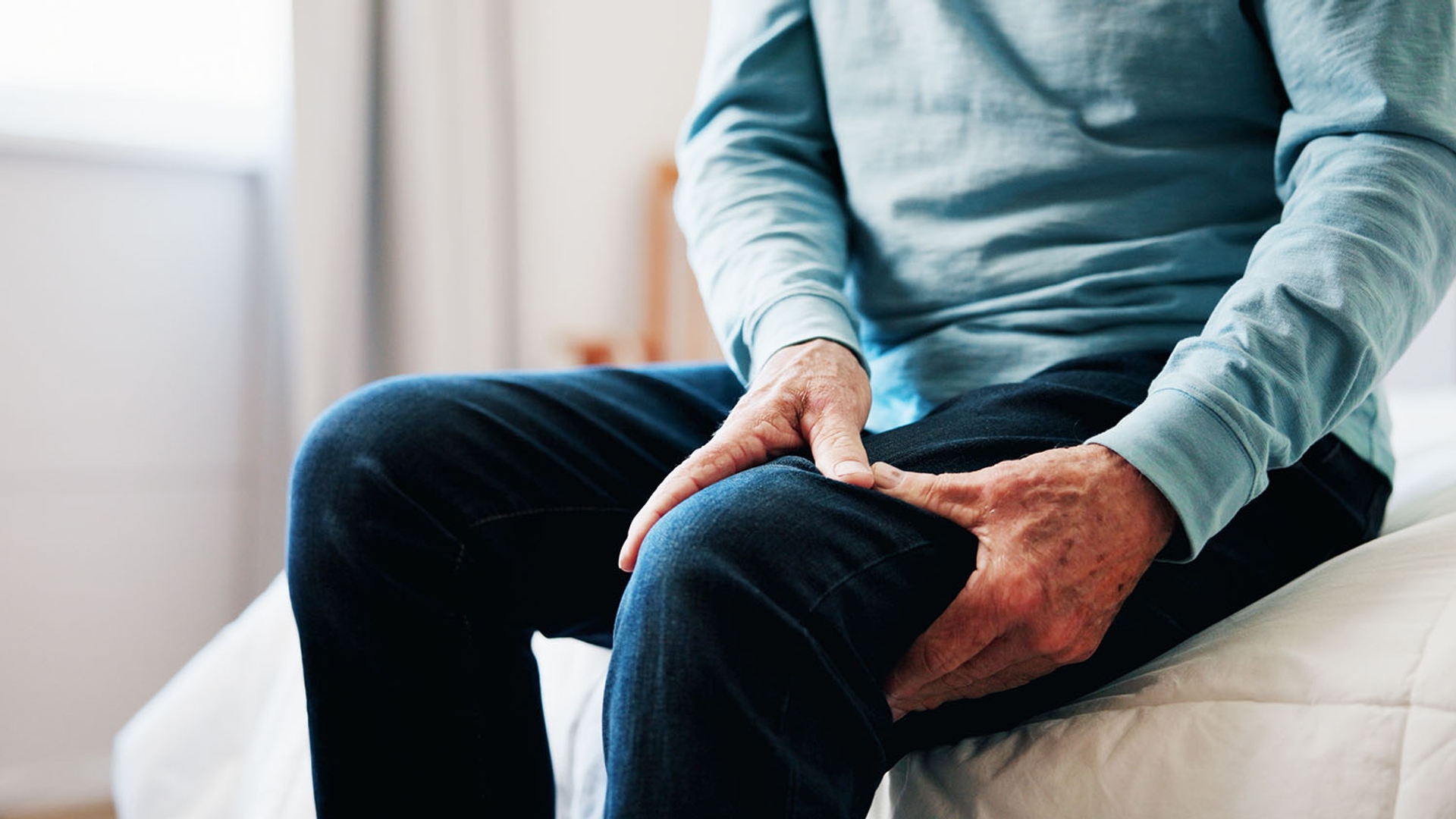 An older person sits and grips their painful thigh.