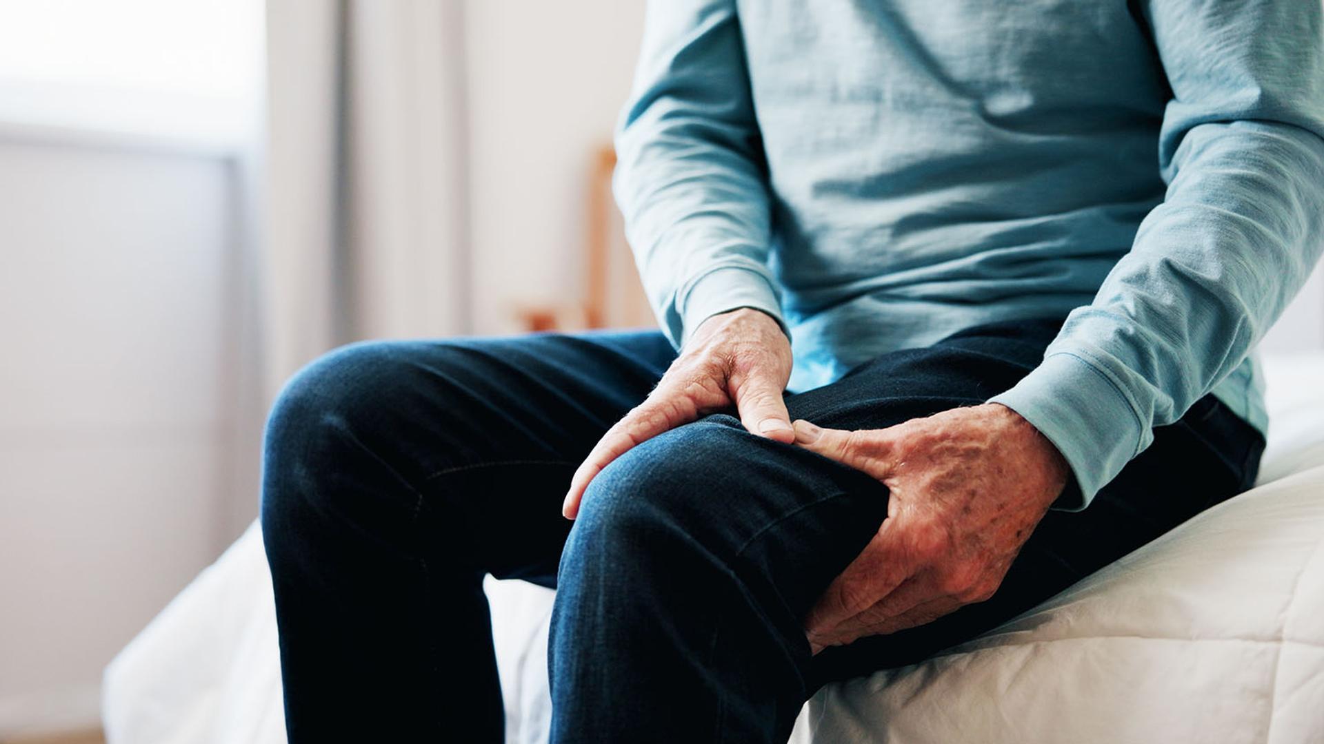 An older person sits and grips their painful thigh.