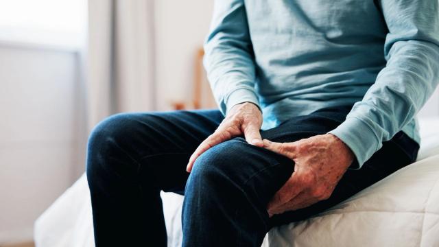 An older person sits and grips their painful thigh.