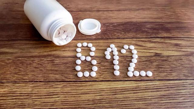 White pill bottle spilling pills that spell out B12 on a wooden surface.