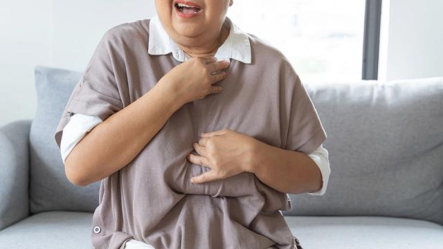 Older person clutching chest and throat in discomfort.