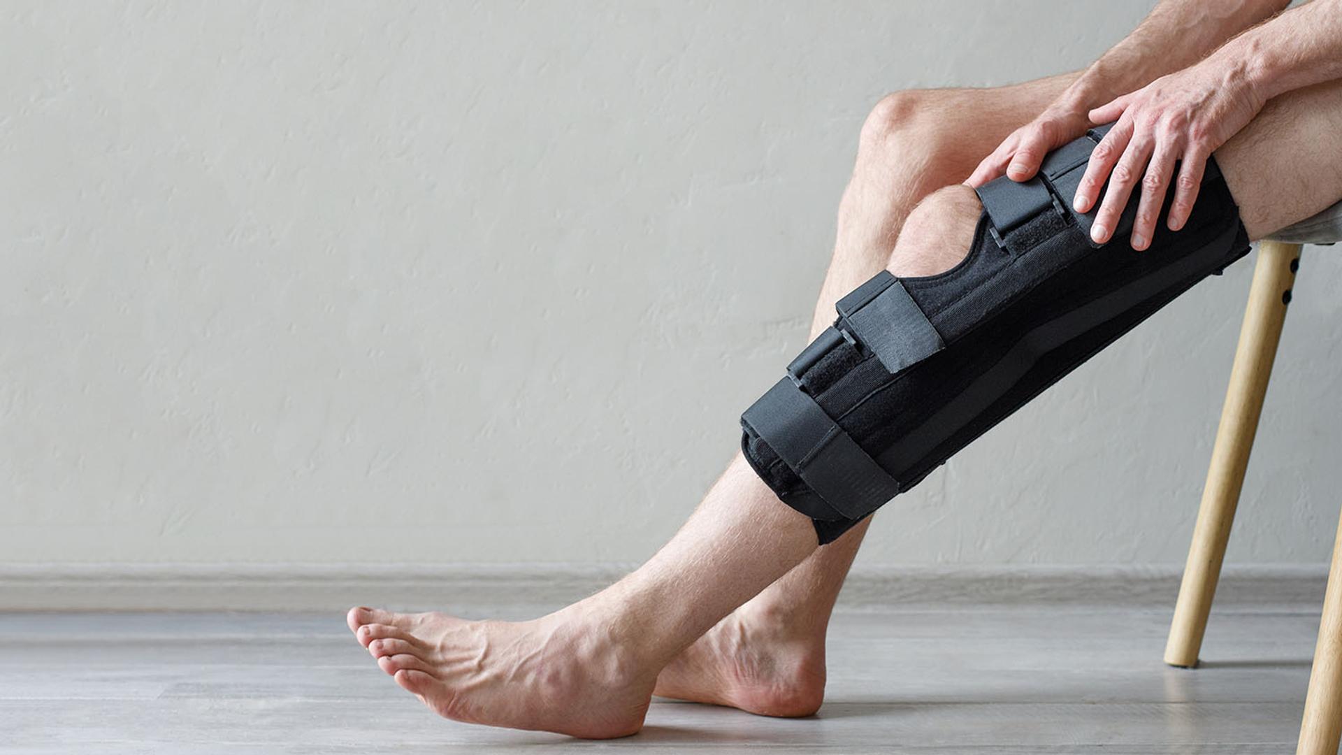 A person sits with a black knee brace on one leg, their hand resting on it.