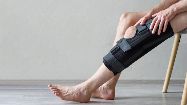 A person sits with a black knee brace on one leg, their hand resting on it.