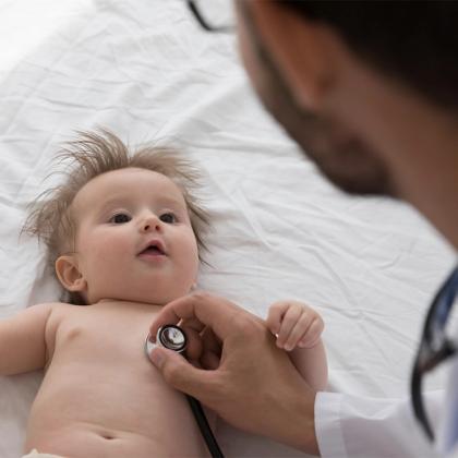 Pediatrician examining a baby with a stethoscope on a white examination table