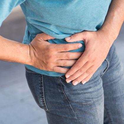Man holding his side, possibly experiencing abdominal pain or discomfort, wearing a blue t-shirt and jeans