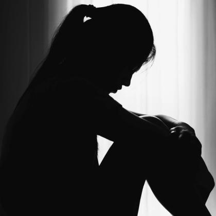 Silhouette of a thoughtful woman sitting with her head bowed down in a dimly lit room