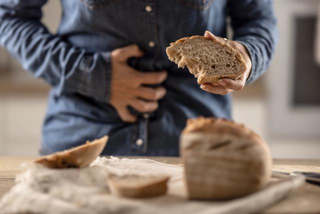 Person clutching stomach in pain while holding a slice of bread.
